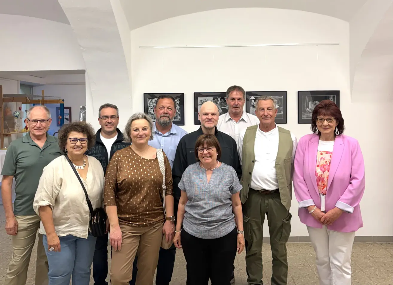 Eine Gruppe von Erwachsenen, darunter Männer und Frauen, stehen in einem Raum mit weißen Wänden und gerahmten Bildern an der Wand. Sie lächeln und posieren für ein Foto.