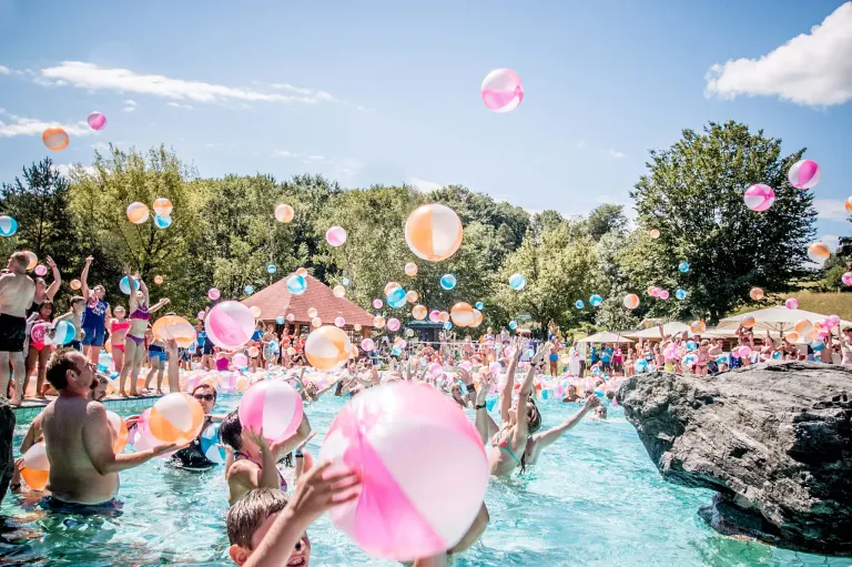 Eine lebhafte Poolparty mit Ballons in der Luft und Menschen, die sich unter einem klaren blauen Himmel vergnügen.