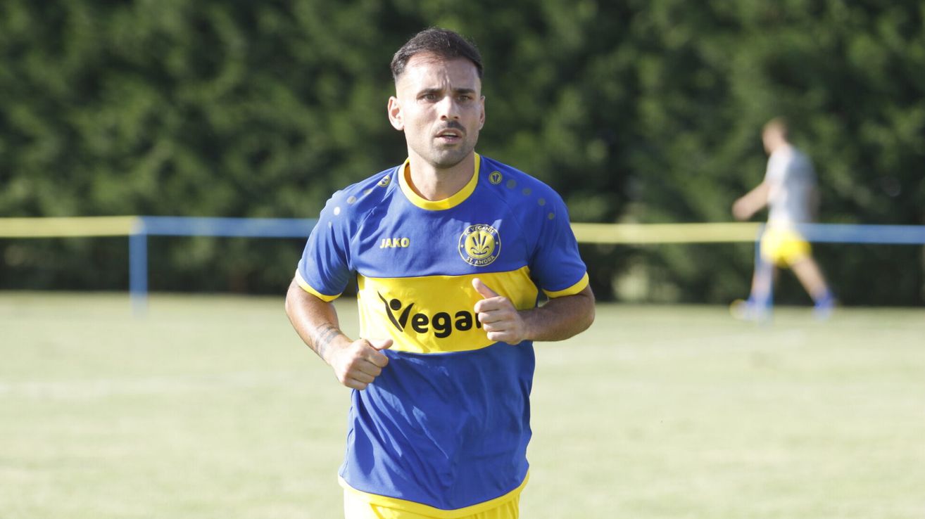 Ein Fußballspieler in blau-gelbem Trikot mit dem Wort 'Vega' läuft auf dem Feld. Der Spieler trägt ein blau-gelbes Trikot mit einem Logo auf der Brust. Der Spieler schaut nach links.