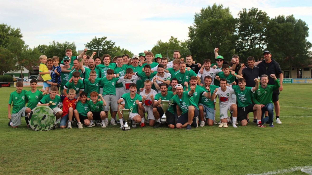 Eine Gruppe junger Männer in grünen Trikots und Mützen feiert einen Sieg auf einem Grasfeld, hält Trophäen und posiert für ein Foto.