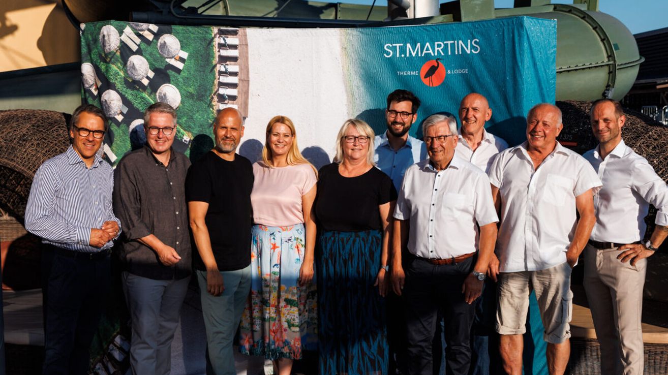 Eine Gruppe von Menschen steht vor einem Banner für St. Martins Therme & Lodge und lächelt für ein Foto.