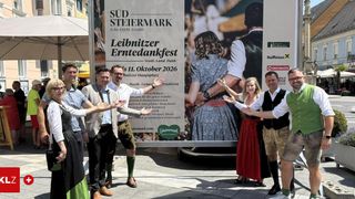 Eine Gruppe von Menschen posiert in traditioneller Kleidung vor einem Banner, das für das Leibnitzer Erntedankfest wirbt.