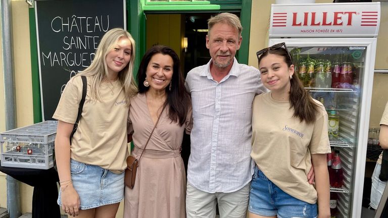 Ein Mann und drei Frauen stehen eng zusammen vor einem Geschäft. Der Mann hat einen Bart und trägt ein helles Hemd. Die Frauen lächeln und eine hat eine braune Tasche.