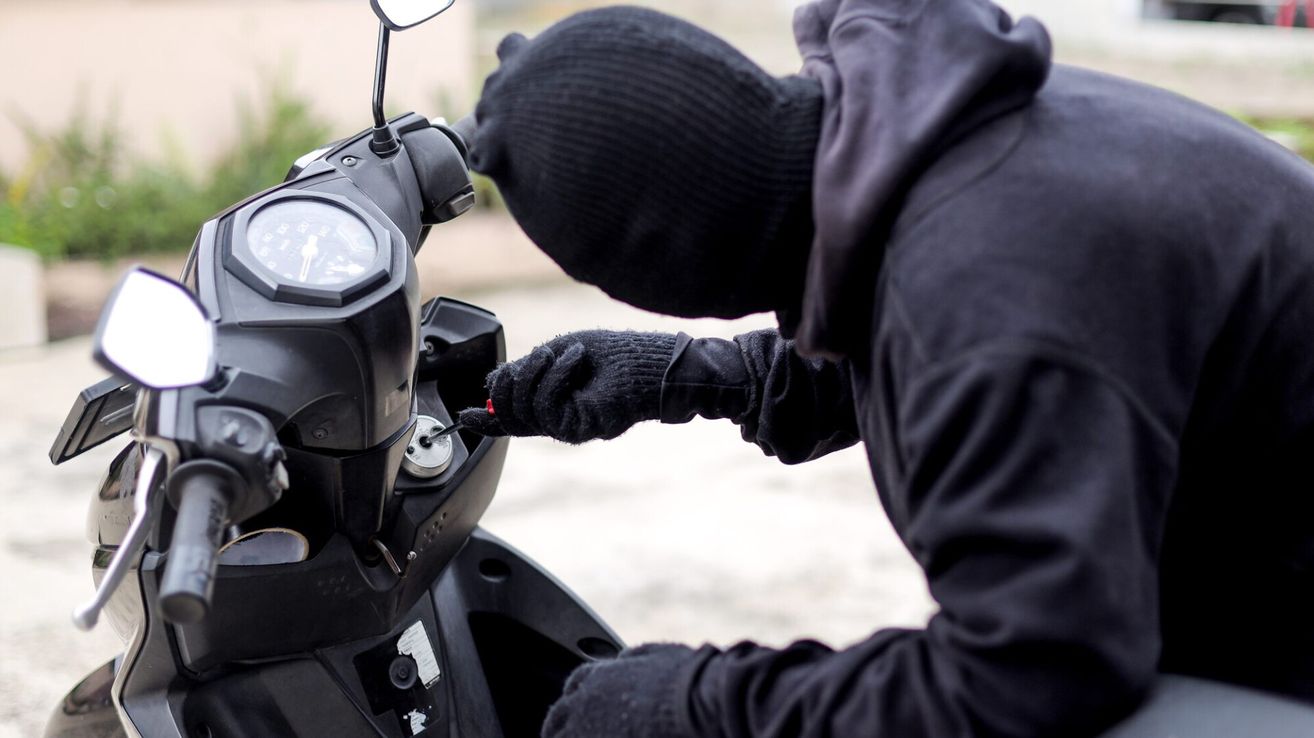 Eine Person in schwarzer Kleidung und Maske versucht, einen Roller mit einem Werkzeug zu öffnen.