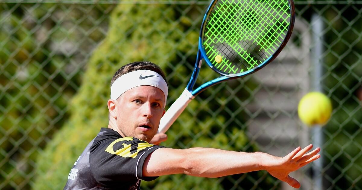 Ein Mann mit einem weißen Nike-Kopfband schwingt einen Tennisschläger, um einen Tennisball zu treffen. Der Schläger ist blau und weiß mit einem gelben Ball darauf.