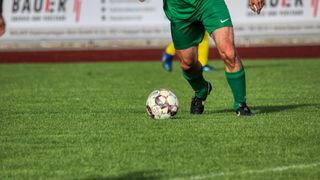 Ein Fußballspieler in einem grünen Trikot läuft auf einem grünen Feld auf einen Ball zu.