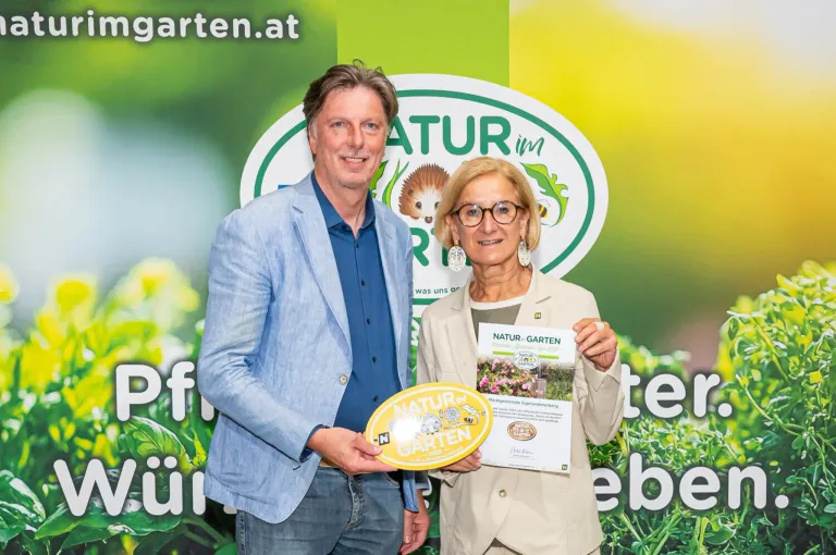 Ein Mann und eine Frau stehen nebeneinander und halten ein Zertifikat mit den Worten 'Natur-Garten'. Sie lächeln und posieren für ein Foto.