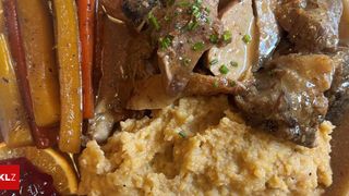 Ein Gericht mit einer reichhaltigen Sauce, bestehend aus gebratenem Fleisch und Gemüse, garniert mit grünen Kräutern.