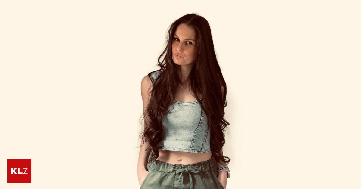 Eine Frau mit langen, welligen Haaren posiert für ein Foto in einem Jeans-Crop-Top und grünen Hosen. Sie hat einen ernsten Ausdruck und schaut geradeaus.