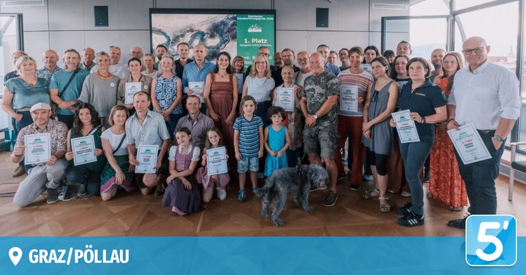 Eine große Gruppe von Menschen in Freizeitkleidung posiert für ein Foto. Sie halten Urkunden in den Händen, und einige tragen Abzeichen. Der Raum hat einen Holzboden und eine grüne Banner im Hintergrund.