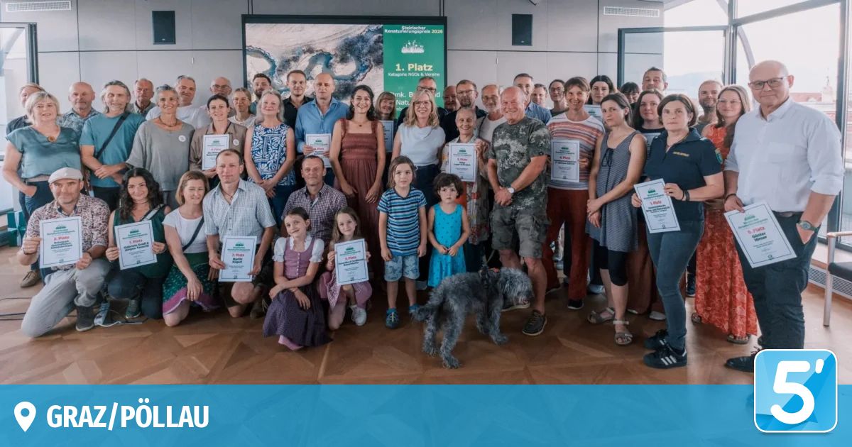 Eine große Gruppe von Menschen in Freizeitkleidung posiert für ein Foto. Sie halten Urkunden in den Händen, und einige tragen Abzeichen. Der Raum hat einen Holzboden und eine grüne Banner im Hintergrund.