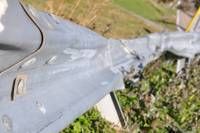 Ein zerbrochenes Stück eines grauen Flugzeugs, wahrscheinlich eines Flugzeugs, liegt auf dem Boden, bedeckt mit Gras und Trümmern.