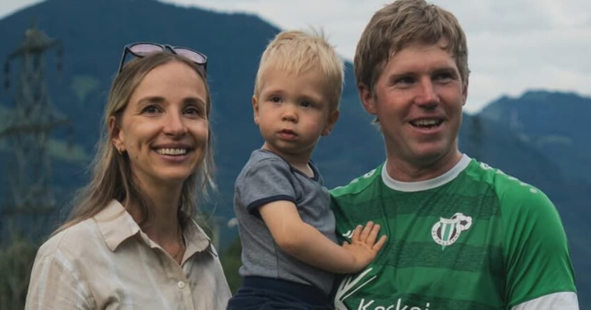 A woman, a smiling boy, and a man in a green jersey are standing outside, with mountains in the background.