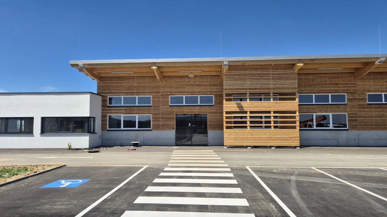 Ein modernes Gebäude mit holzverkleideten Außenwänden und Glasfenstern steht unter einem klaren blauen Himmel in einem Außenbereich.