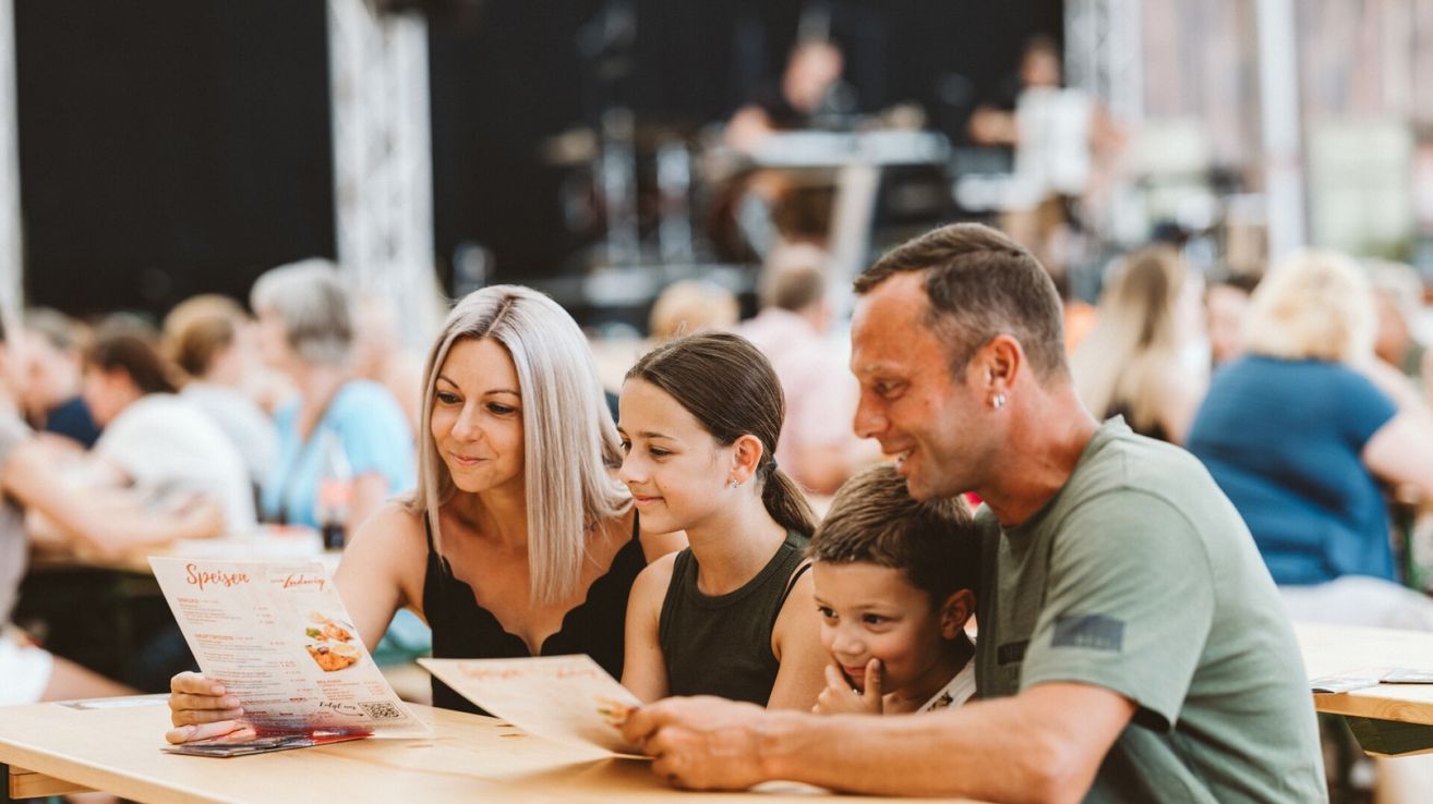 Eine Familie liest eine Speisekarte an einem Tisch in einem Restaurant mit verwaschenem Hintergrund von Menschen und einer Band.