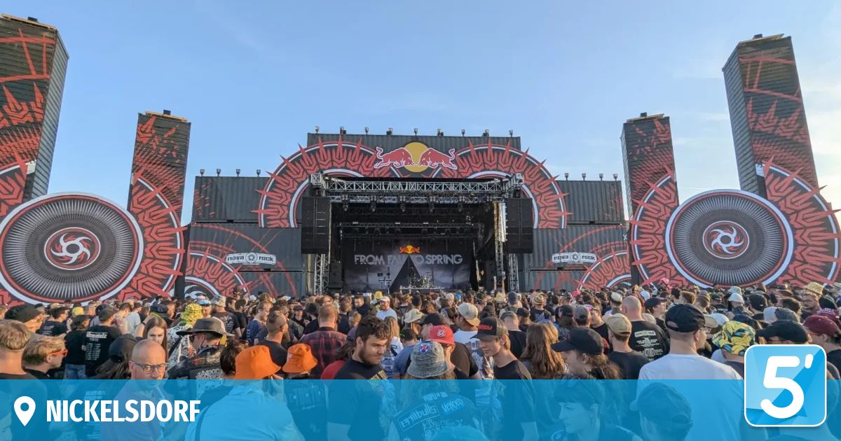 Eine große Menschenmenge versammelt sich vor einer Bühne mit einem prominenten Bullenlogo, wahrscheinlich bei einem Musikfestival. Die Bühne ist gut beleuchtet, und es sind Lautsprecher und Beleuchtungsausrüstung zu sehen.