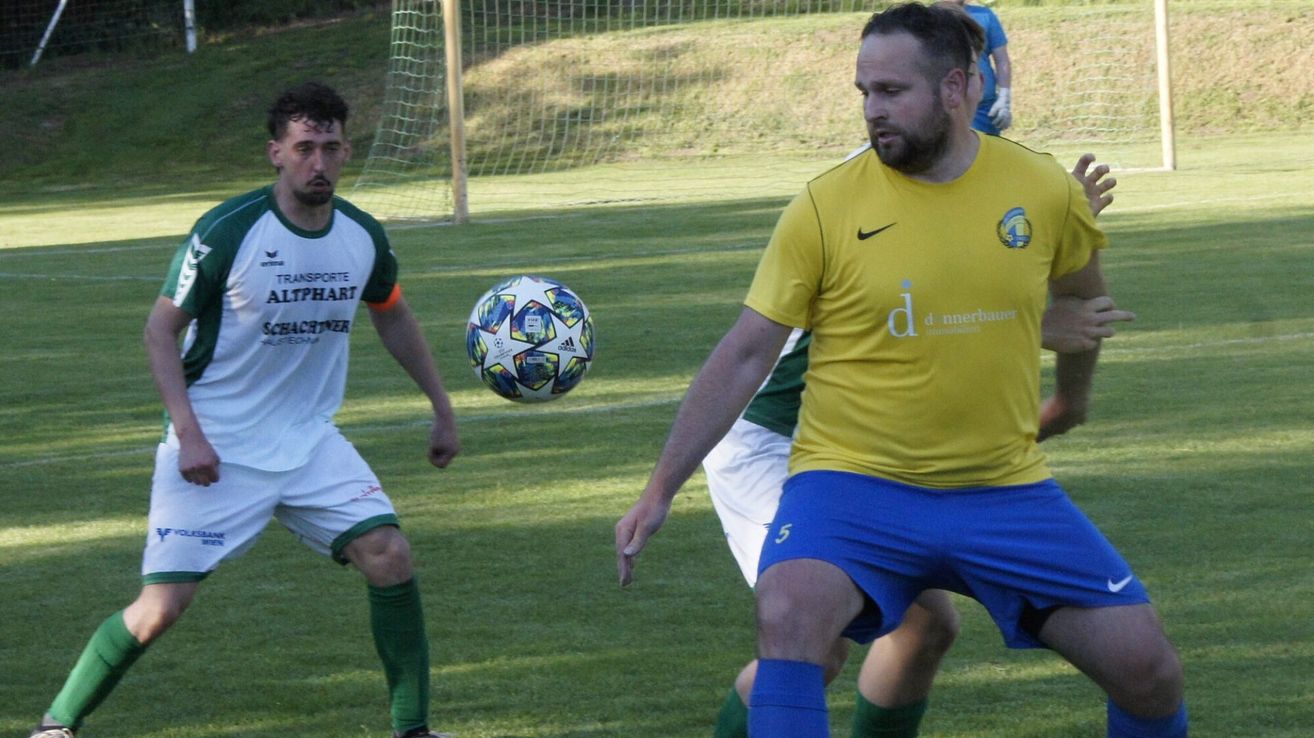 Two soccer players are in the middle of a match. One player is wearing a green and white uniform and the other is in a yellow and blue uniform. A soccer ball is in the air.