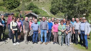 Eine Gruppe von Erwachsenen steht vor einem Haus mit einem Berg im Hintergrund. Sie alle lächeln und scheinen für ein Foto zu posieren.