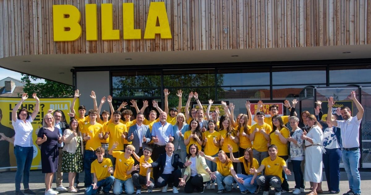 Eine Gruppe von Menschen in gelben T-Shirts posiert für ein Foto vor einem BILLA-Geschäft. Sie lächeln und heben die Hände.