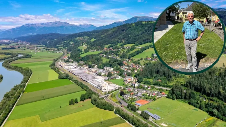 Eine Luftaufnahme eines grünen Tals mit einer Fabrik und Häusern, Bergen in der Ferne und einem Tennisplatz.