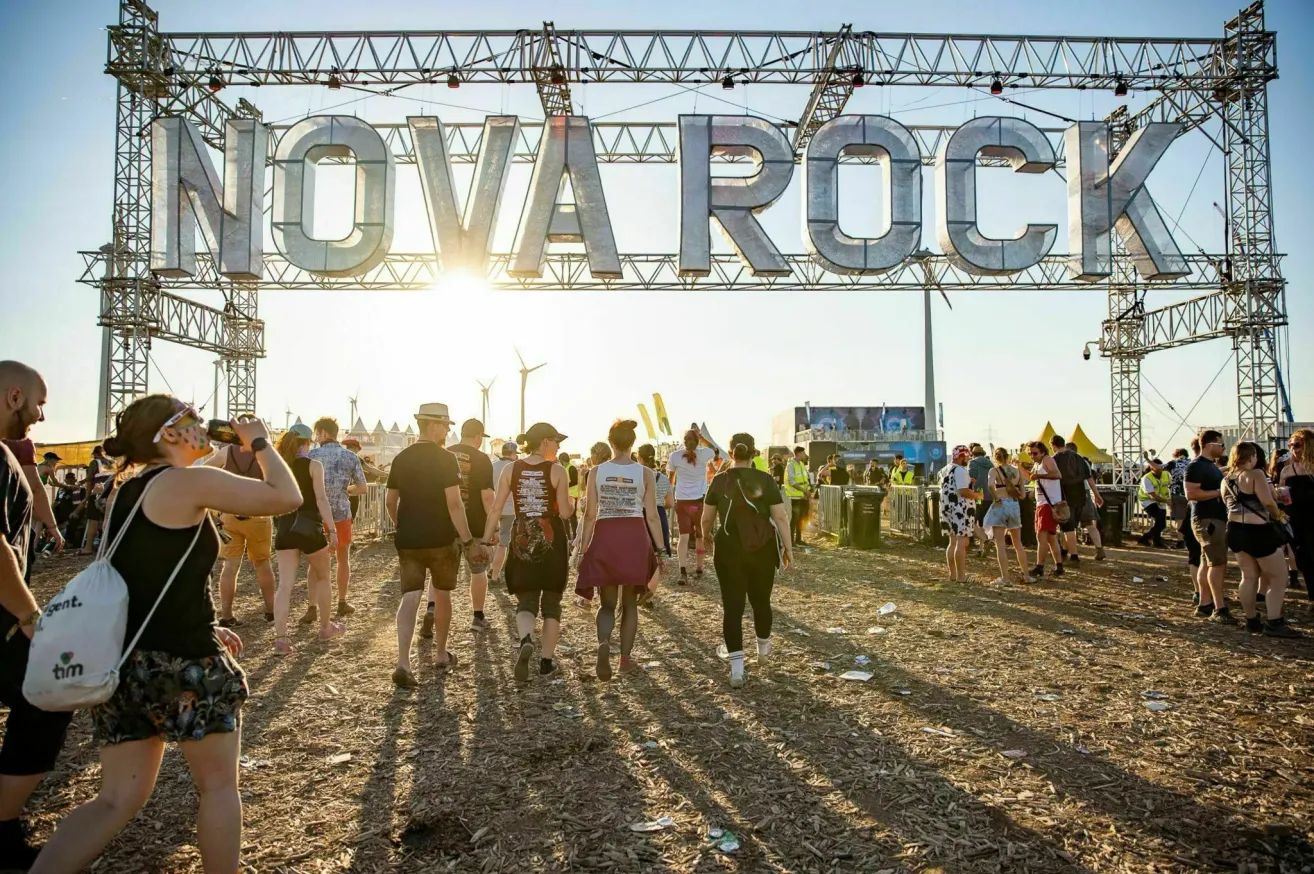 Viele Menschen gehen vor dem Eingang zum Nova Rock Festival. Die Sonne scheint und die Schatten der Menge werden auf den Boden geworfen.