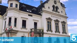 The Rathaus building features a white exterior with black roofing, several arched windows, and flags on poles in front. The word Rathaus is prominently displayed above the entrance.