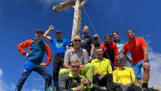 Eine Gruppe von Wanderern steht auf einem Berggipfel und posiert fr ein Foto mit einem hölzernen Kreuz im Hintergrund.