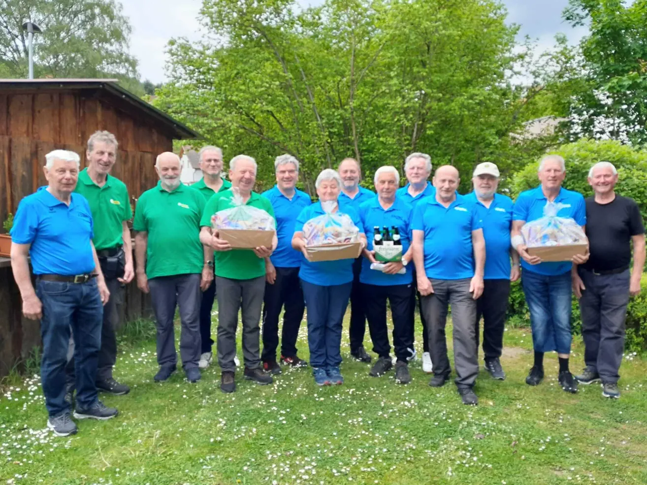 Eine Gruppe von Menschen in passenden Uniformen, einige in Grün und einige in Blau, posiert für ein Foto auf einer Rasenfläche mit Bäumen im Hintergrund. Einige von ihnen halten Körbe.