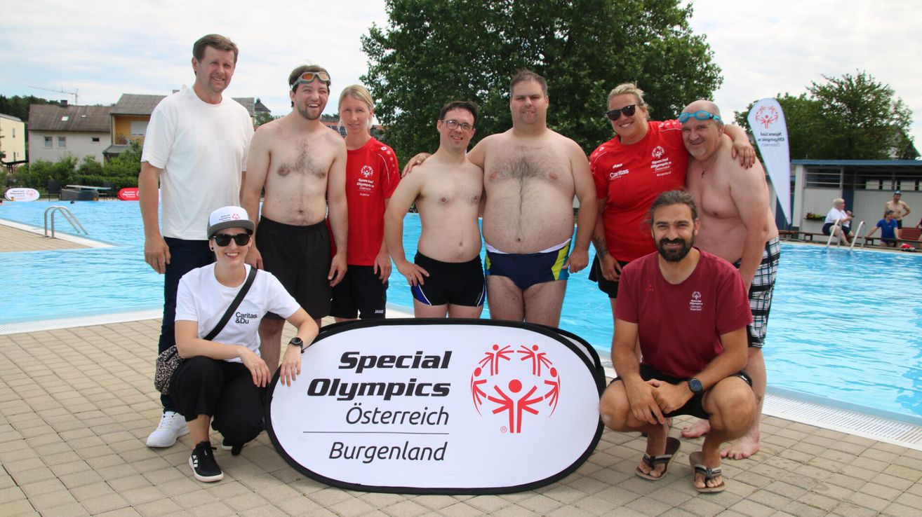 Eine Gruppe von Personen, sowohl Männer als auch Frauen, posiert für ein Foto vor einem Pool. Der Hintergrund zeigt das Logo der Special Olympics Österreich Burgenland.