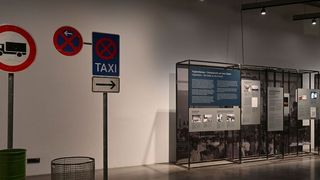 A museum exhibit with a taxi sign, a no-truck sign, and informational panels.