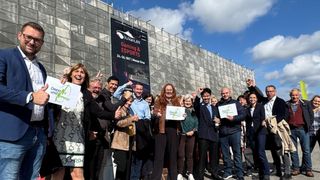 A group of people pose for a photo in front of a building advertising 'Gaming & Esports'. They hold signs and appear to be celebrating.