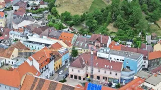 A town with many buildings, some under construction, set against a backdrop of lush green hills and a prominent clock tower.