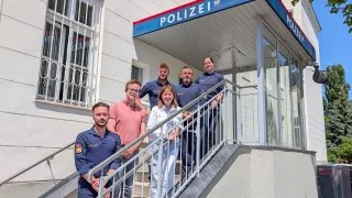 Five police officers, including one woman, pose for a photo on the steps of a police station.
