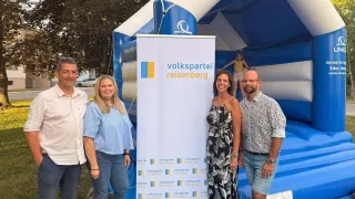 Four people stand in front of a Volkspartei Reisenberg banner, near an inflatable castle with an Eden Andreas logo, smiling for a photo.