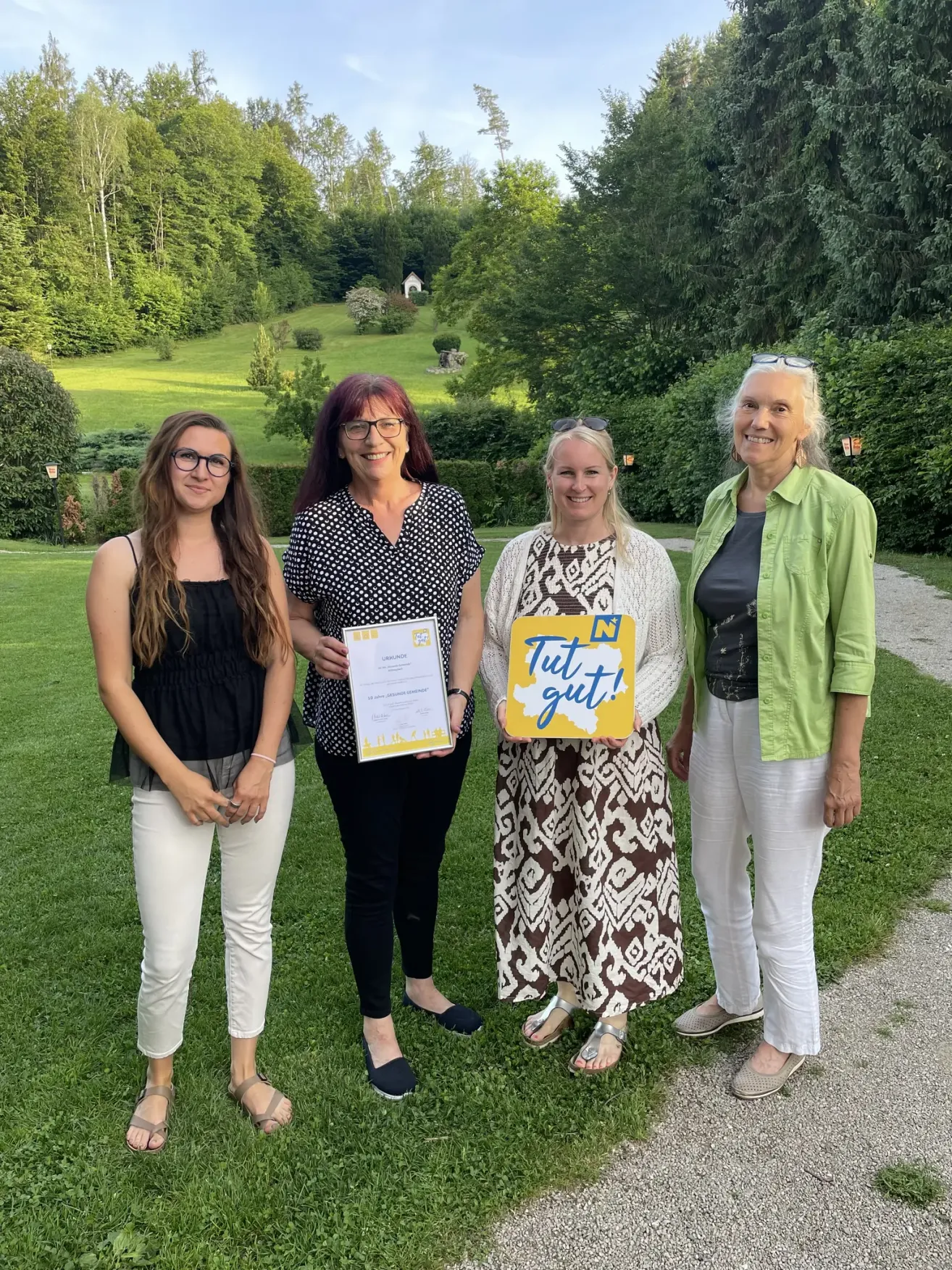 Four women stand on a lawn, smiling, holding certificates and a yellow sign that says Tut gut!