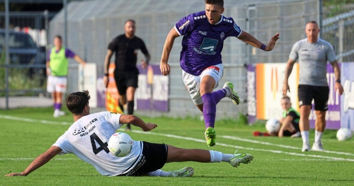A soccer player in purple makes a slide tackle on another player wearing white. The player in white wears the number 4.