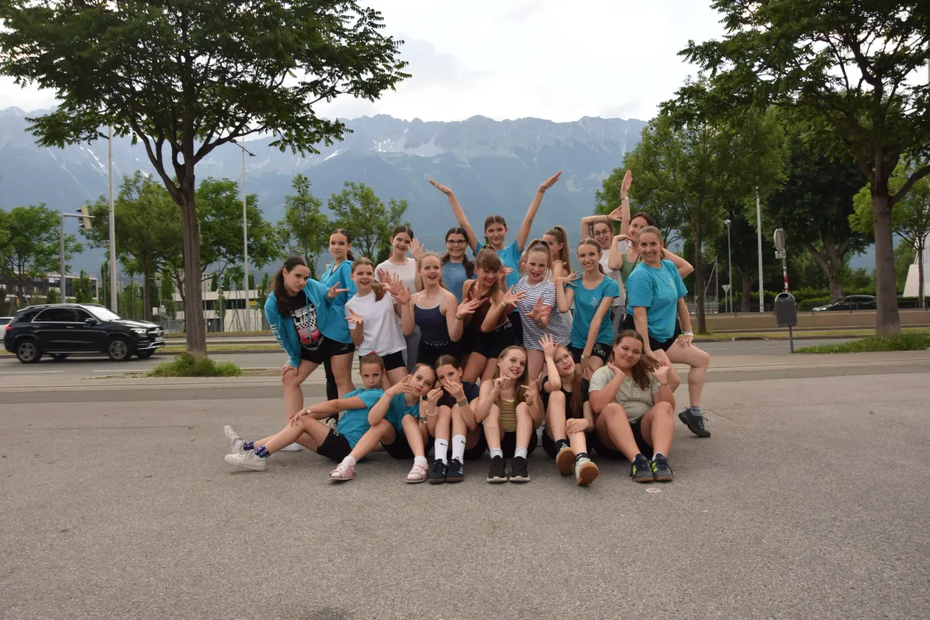 A group of girls in matching blue shirts are posing for a picture on a road with mountains in the background.