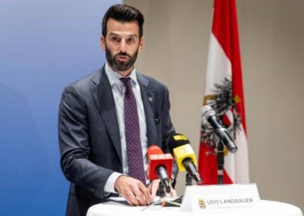 Ein Mann steht an einem Podium mit Mikrofonen vor ihm, möglicherweise bei einer Pressekonferenz.