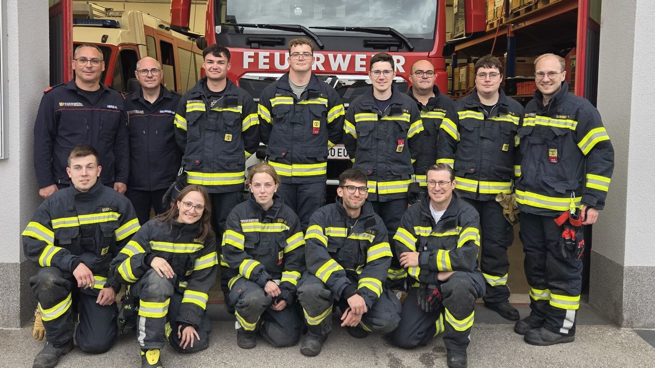 A group of firefighters, both men and women, are posing for a photo in front of a fire truck. They are all wearing their uniforms.