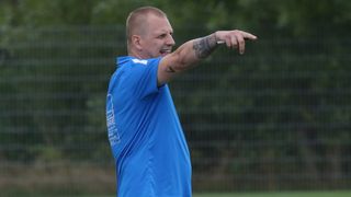 A man in a blue shirt with white text and a tattoo on his arm points with his index finger.