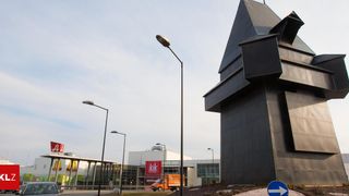 A building with a triangular roof is in front of a McDonald's and a KIK store. There is an orange truck and street lights.