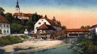 A vintage image shows a riverside house with a wooden bridge, surrounded by trees and a distant tower.
