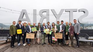 A group of people stand together, holding gift certificates and flowers. They pose for a photo in front of a large sign with the word Airyt.
