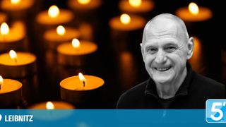 A smiling man stands against a background of lit candles, signifying a memorial or remembrance event.