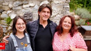 A man and two women standing in front of a stone wall with faces carved into it, smiling and posing for a photo.