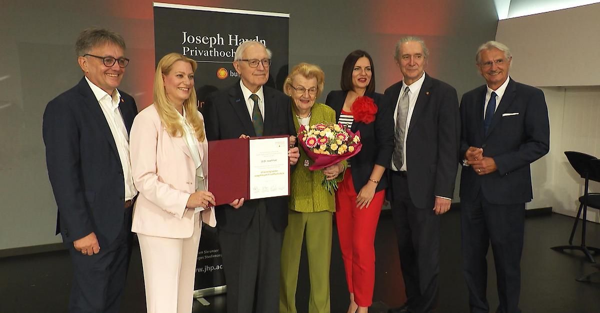A group of people holding flowers and a certificate at an award ceremony. A banner with Joseph Haydn Privathoch appears behind them.