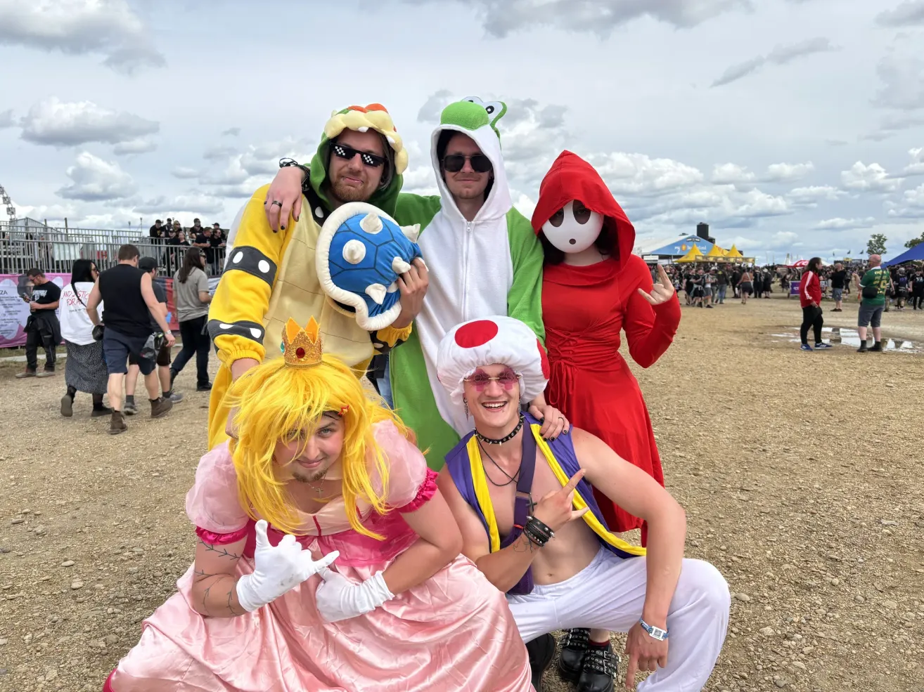 Gruppe von Freunden in Nintendo-Charakter-Kostümen posiert für ein Foto bei einer Outdoor-Veranstaltung. Einer ist eine Prinzessin, andere in Toad, Mario und Bowser Kostümen.