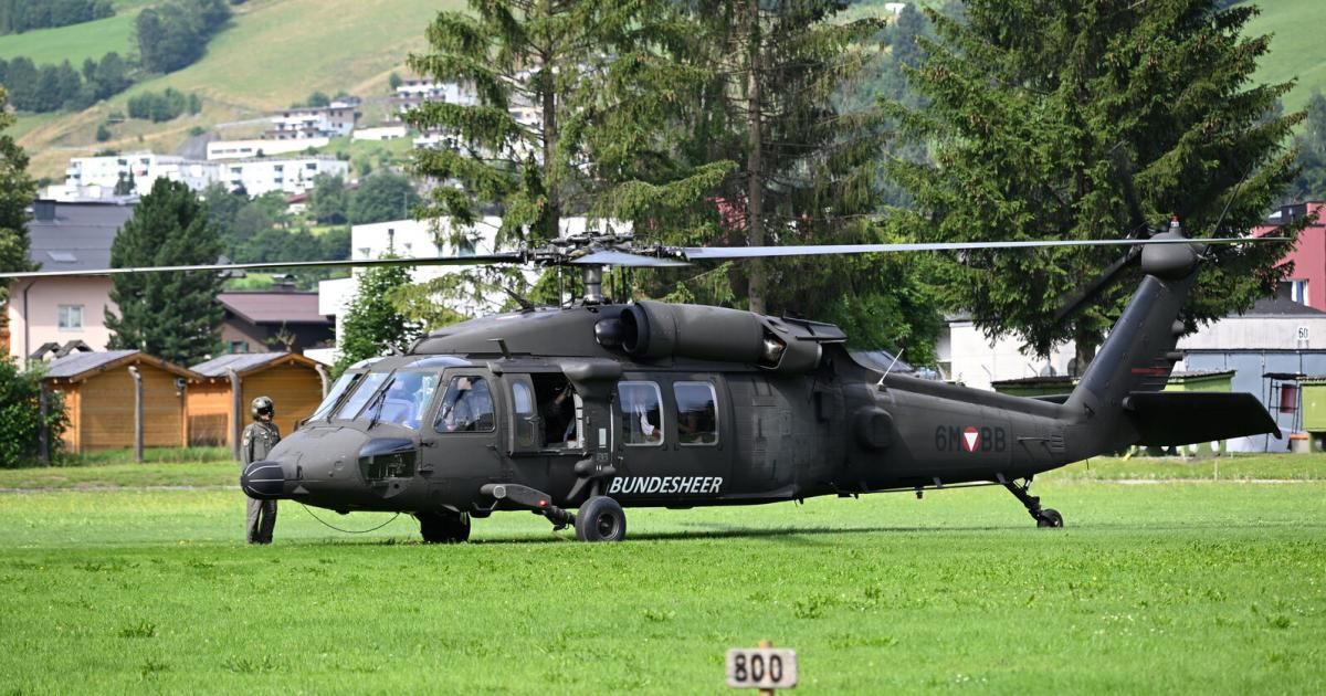 Ein schwarzer Militärhubschrauber mit der Aufschrift Bundesheer ist auf einem Grasfeld geparkt, mit Gebäuden im Hintergrund.