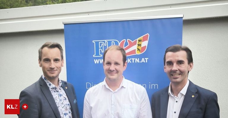 Drei Männer stehen vor einem blauen Banner. Die zentrale Figur trägt ein weißes Hemd, während die anderen Anzüge tragen. Das Banner zeigt ein Logo mit 'FW' und 'WKTN.AT'.