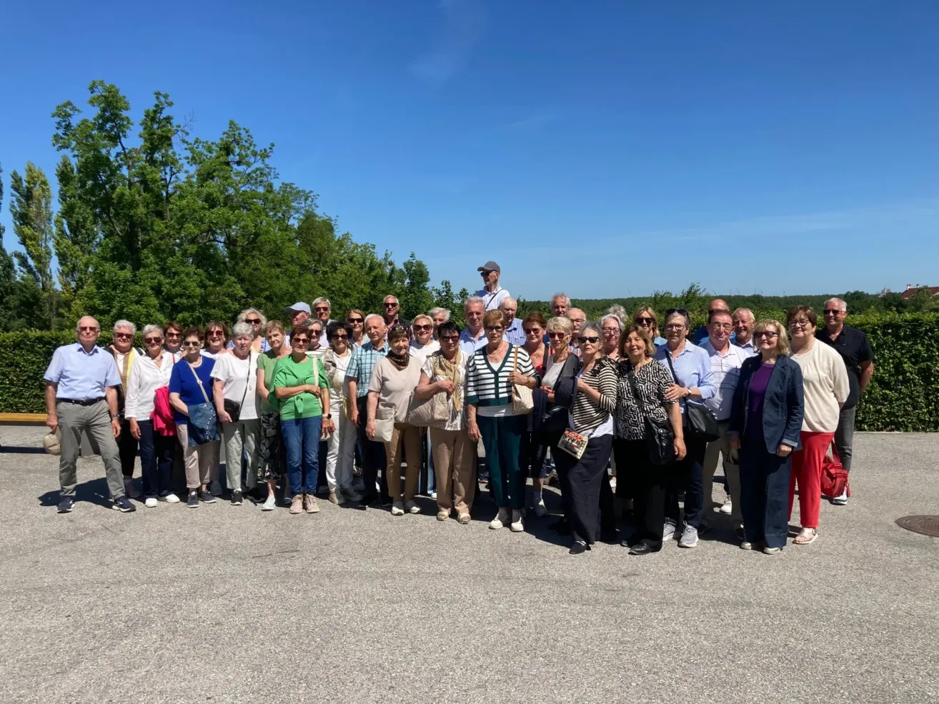 Eine Gruppe von Erwachsenen, wahrscheinlich auf einer Reise, steht für ein Foto in einer Reihe mit Bäumen und blauem Himmel im Hintergrund.